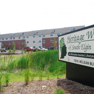 A senior living facility with a sign in front and surrounding greenery.