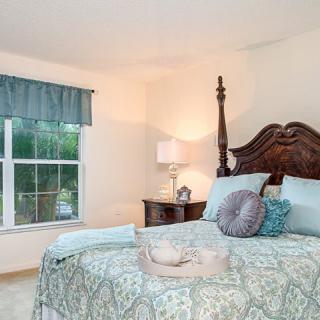 A cozy bedroom featuring a large bed with patterned bedding, a bedside table with a lamp, and a window with curtains.
