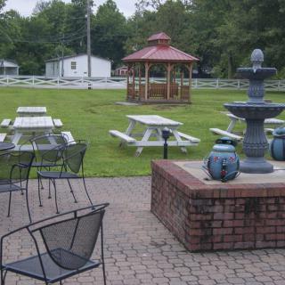 A peaceful outdoor patio area featuring picnic tables, a gazebo, and a decorative fountain.