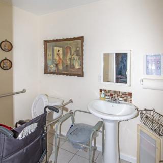 An accessible bathroom equipped with a wheelchair, handrails, and a pedestal sink beneath a mirror.