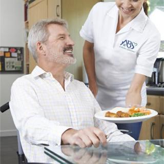 A caregiver serves a meal to an elderly man in a wheelchair.
