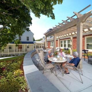 A pleasant outdoor patio with a pergola, where seniors are seated and enjoying their time in a garden setting.