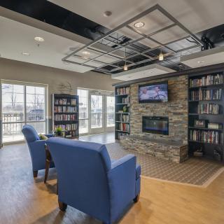 A modern library with comfortable seating, a stone fireplace, and bookshelves lining the walls.