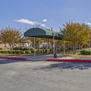 A covered entrance with a green canopy in front of a building surrounded by trees and a parking lot.