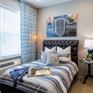 A cozy bedroom featuring striped bedding, decorative pillows, and a stylish lamp beside a tufted headboard.
