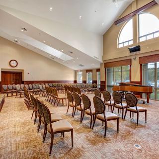 A spacious conference room with rows of chairs and a grand piano near large windows.