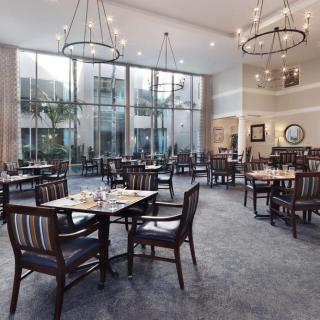 A spacious, well-lit restaurant dining area with empty tables and elegant chandeliers.