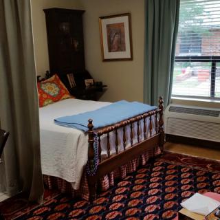 A cozy bedroom with a wooden bed, patterned carpet, and large window.