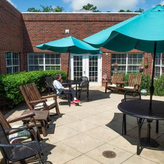 A sunny outdoor patio with chairs and umbrellas next to a brick building.