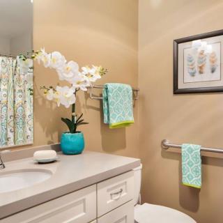 A well-decorated bathroom with a light color scheme, featuring a sink, mirror, orchid in a vase, and colorful towels.