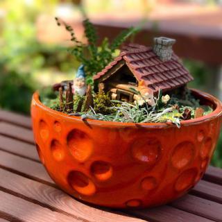 A charming miniature garden with a wooden house model in a decorative orange planter.