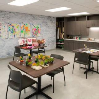 A modern workspace featuring tables and chairs with colorful artwork on the wall.