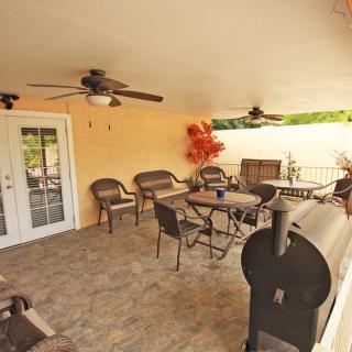 A cozy covered patio with tables, chairs, ceiling fans, and a barbecue grill.