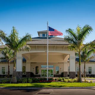 A modern building entrance with palm trees and an American flag.