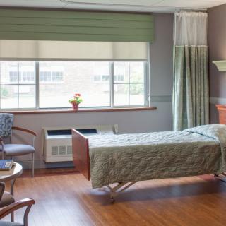 A hospital room with a bed next to a large window and chairs.