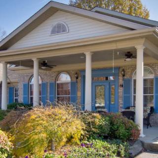 A charming house with a spacious porch supported by white columns, surrounded by a vibrant garden and featuring blue shutters.