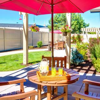 A sunny outdoor patio with a table and chairs under a red umbrella, featuring a pitcher of lemonade.