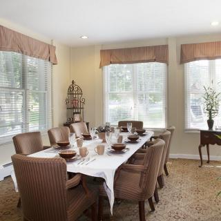 A well-lit dining room with a large table set for a meal, surrounded by chairs and adorned with elegant decor.
