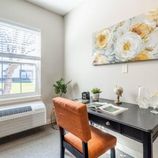 A cozy home office setup featuring a desk, an orange chair, and floral artwork.