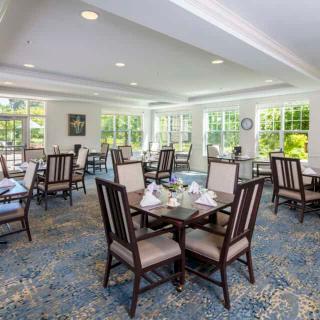 A well-lit dining room with several tables and chairs arranged neatly on a carpeted floor.