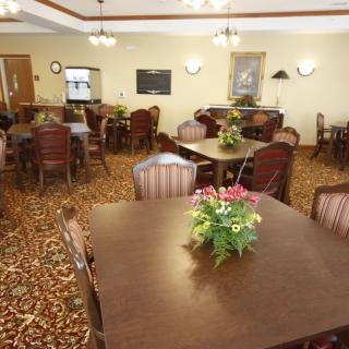 A cozy dining area with multiple tables and chairs, decorated with flowers and lit by warm overhead lighting.
