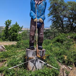A large statue of a man standing on a tree stump, surrounded by greenery.