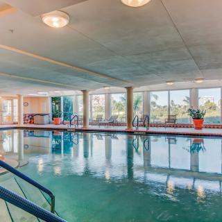Modern indoor swimming pool with large windows and bright lighting.
