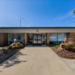 Entrance of a building with a pathway and surrounding landscaping under a clear blue sky.