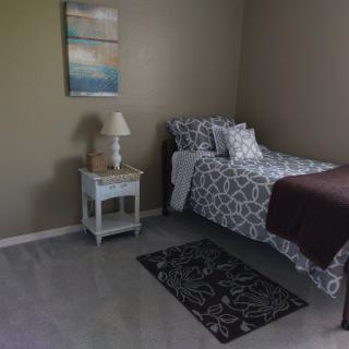 A simple, well-lit bedroom with a single bed and nightstand.