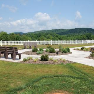 A scenic outdoor park with benches, walking paths, and lush greenery against a backdrop of hills.