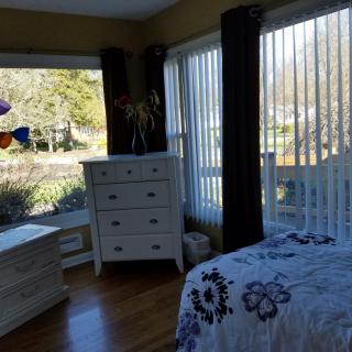 A cozy bedroom with large windows, a white dresser, and a bed decorated with purple floral bedding.