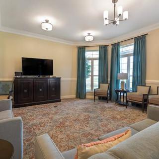 A cozy living room featuring a television, plush chairs, and elegant curtains framing the windows.