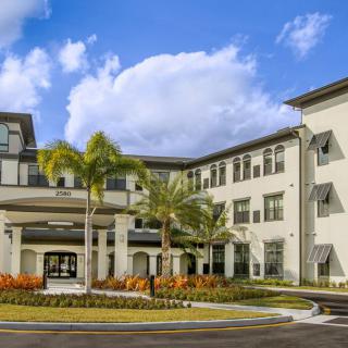 A modern building with palm trees and landscaped grounds under a partly cloudy sky.