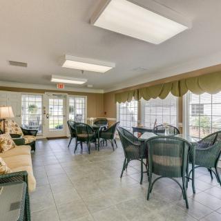 A well-lit community room featuring tables and chairs, with large windows allowing natural light.