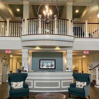 A spacious and elegant hotel lobby featuring a central chandelier, seating area, and grand staircase.