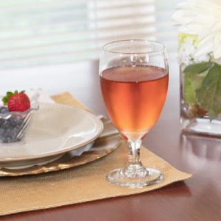 A dining table with a glass of ros� wine and a place setting featuring a plate and strawberry.