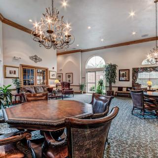 A spacious and elegant living room featuring a large wooden table and chairs, with chandeliers and tasteful decor.
