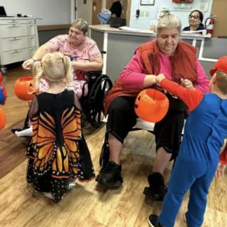 Children in Halloween costumes interacting with seniors during a community event.