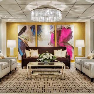 A modern living room with elegant furnishings, featuring a central chandelier and vibrant artwork.