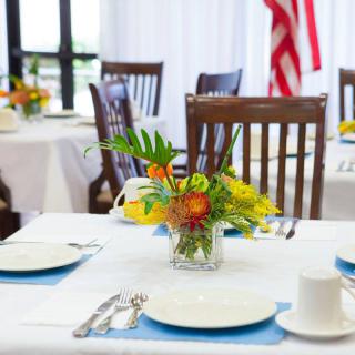 A formally set dining table with a floral centerpiece and an American flag in the background.