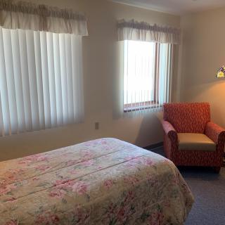 A cozy bedroom with a floral-patterned bedspread, featuring a cushioned armchair by the window.