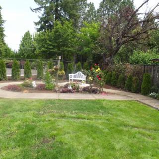 A well-maintained garden with a bench, surrounded by trees and a grassy lawn.