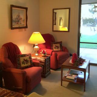 A cozy living room with red armchairs, a lamp, and a wooden table near a window.