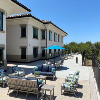 A sunny outdoor patio with comfortable seating and umbrellas beside a building.