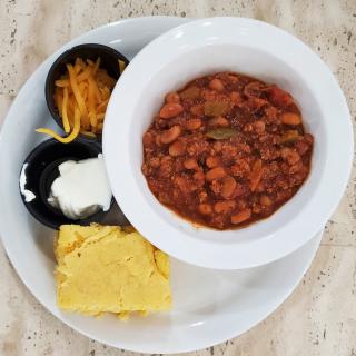 A hearty meal featuring a bowl of chili accompanied by cornbread, shredded cheese, and sour cream.