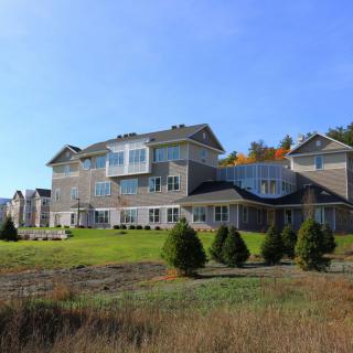A large residential building with a well-maintained lawn and trees on a sunny day.