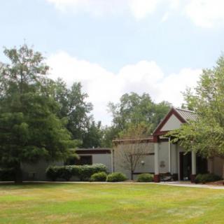 A residential house surrounded by trees and a well-maintained lawn under a clear sky.