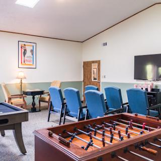 A cozy game room featuring a foosball table, a pool table, comfortable blue seating, and a TV for entertainment.