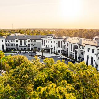 Aerial view of a modern apartment complex surrounded by lush trees at sunset.