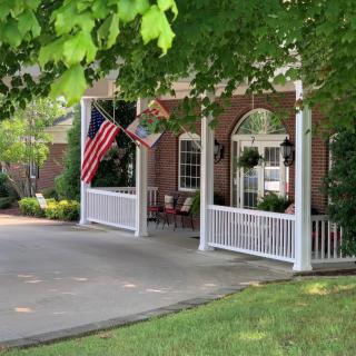 A house with a porch adorned with flags and surrounded by greenery.